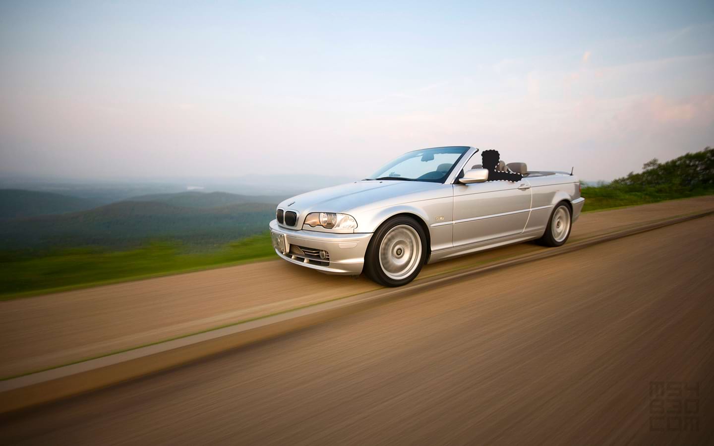 A motion shot of the E46 and driver with the top down driving along mountain ridgelines.