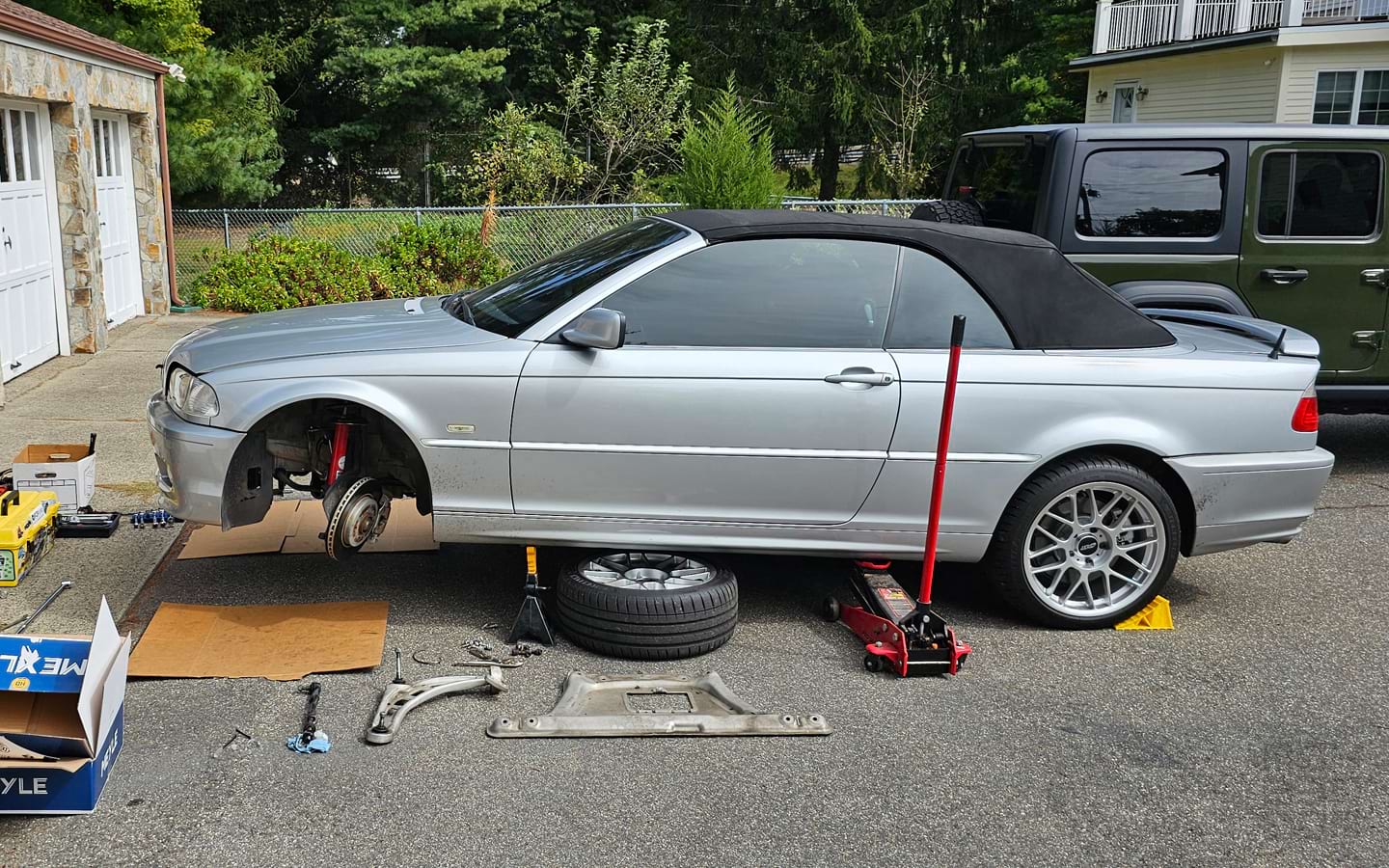 Suspension repairs being done with the front of the vehicle jacked up in a driveway.