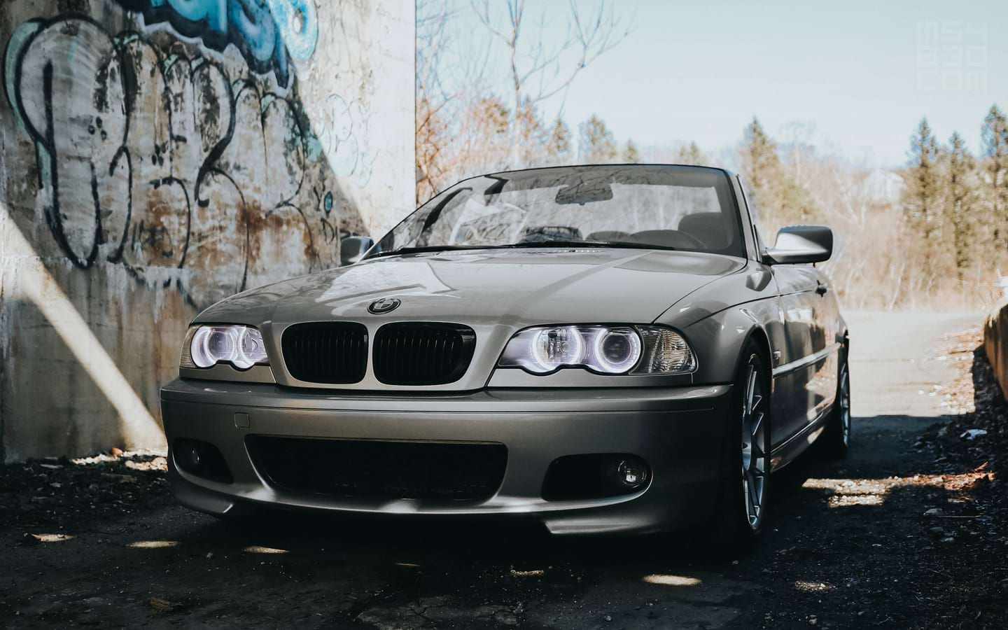 My E46 parked in shadows under a bridge with a vibrant blue sky in the background.