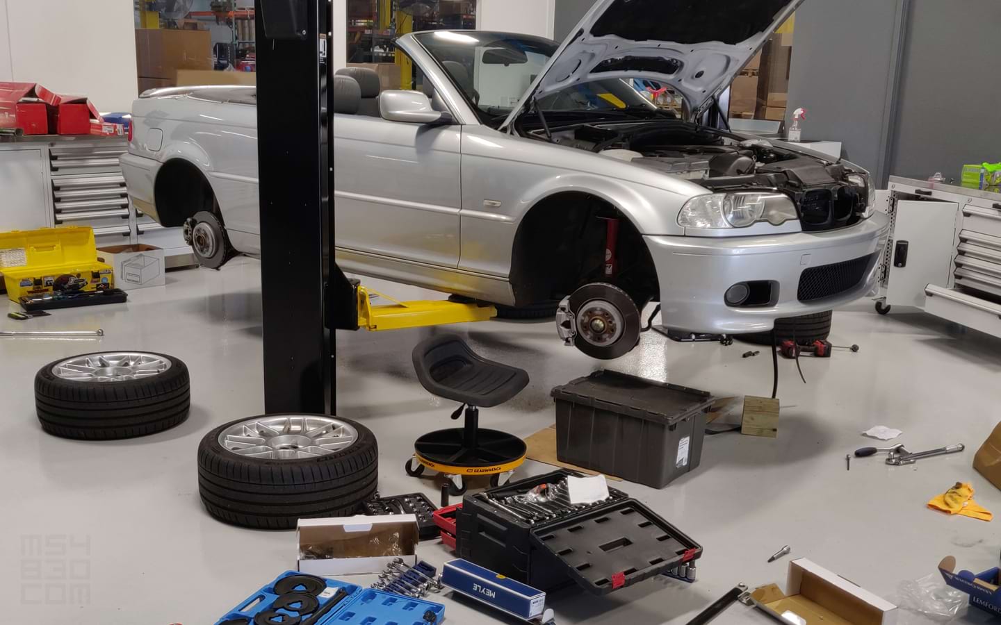 Suspension repairs being done with the E46 on a lift in a professional motorsport garage.