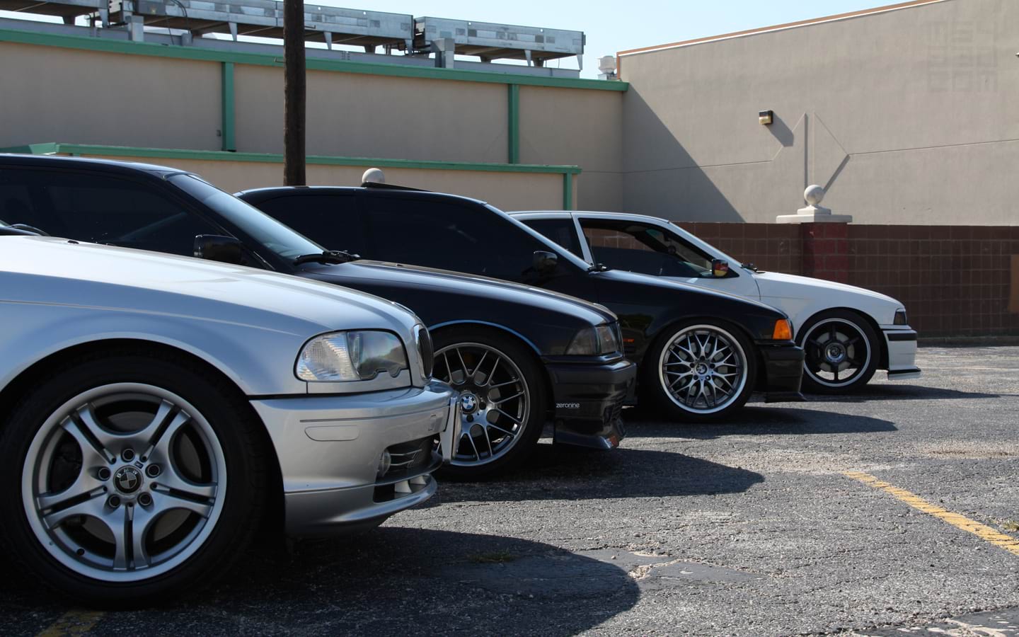 Four classic BMWs at a car meet parked in a staggered formation with front wheels showing.