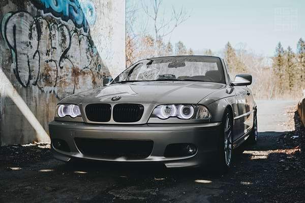 My E46 parked in shadows under a bridge with a vibrant blue sky in the background.