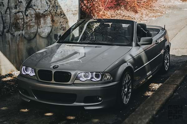 Front and driver side of the E46 parked in shadows with fall colors in the background.