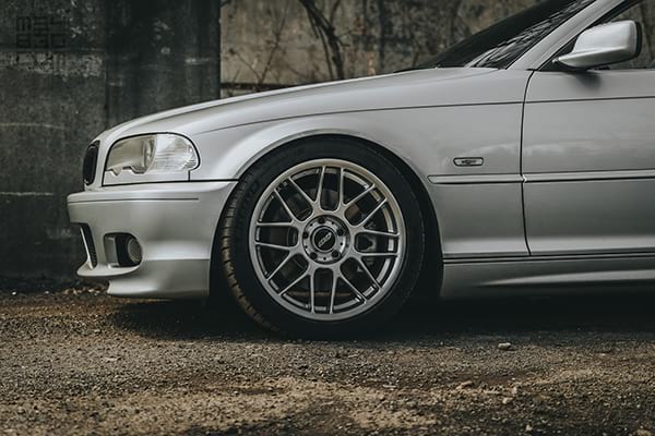 Close-up of the Apex ARC-8 front driver wheel with the E46 parked on a gravel road.