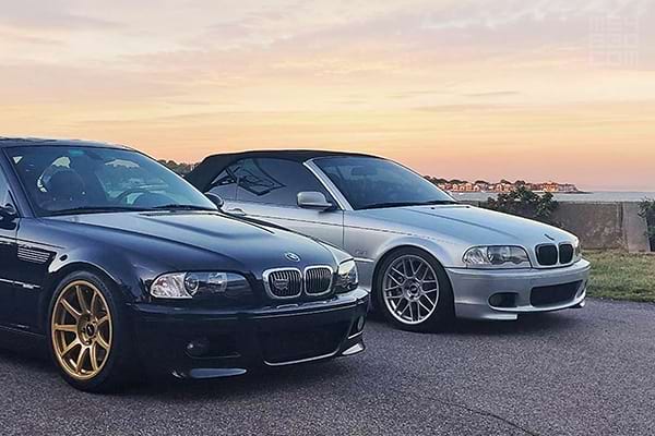 A friend's midnight blue E46 M3 next to my silver 330Ci convertible in front of an ocean sunset.