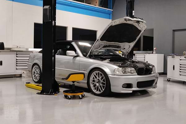 The E46 parked in a professional motorsports garage with the hood open ready for repairs.