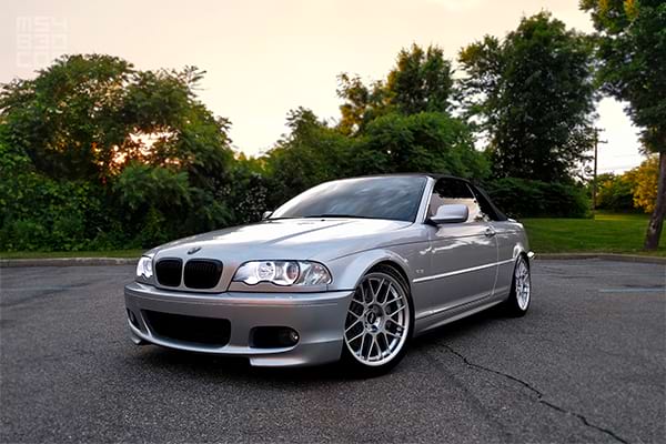 The front and driver side of my E46 in front of trees and a faint setting sun.