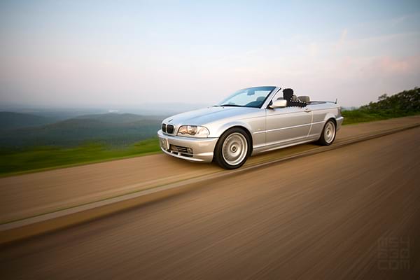 A motion shot of the E46 and driver with the top down driving along mountain ridgelines.