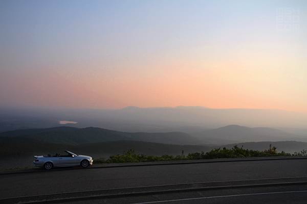 The E46 parked in the distance overlooking a mountain range with a sunset filling the sky.