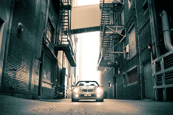 The E46 parked in a downtown alleyway with fire escapes and industrial buildings on either side.